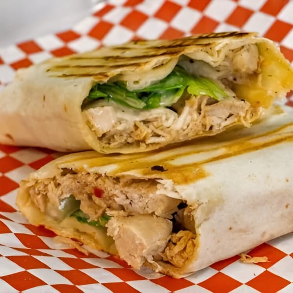 Two halves of a grilled chicken wrap with lettuce and sauce on red and white checkered paper.
