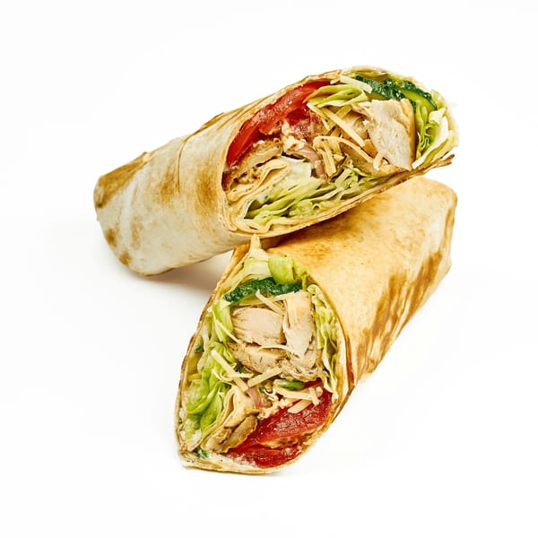 Two halves of a chicken wrap, filled with lettuce, tomatoes, cheese, and sauce, on a white background.