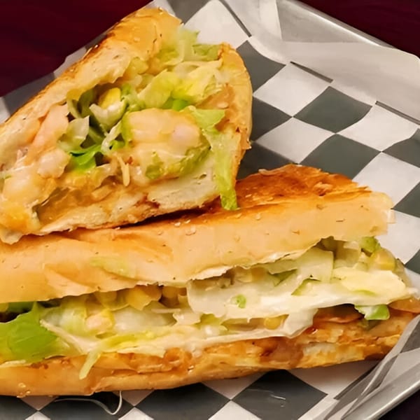 Two halves of a toasted AlBasha chicken sub sandwich with lettuce and sauce on checkered paper.