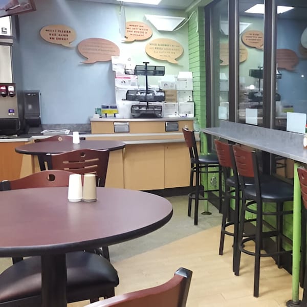 Interior of AlBasha Subs with dining tables, chairs, and a counter with bar stools.