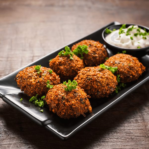 Six crispy falafel patties garnished with parsley, served with a side of white sauce.