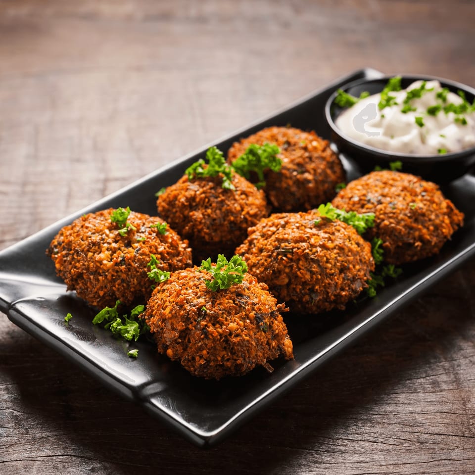 Six crispy falafel patties garnished with parsley, served with a side of white sauce.