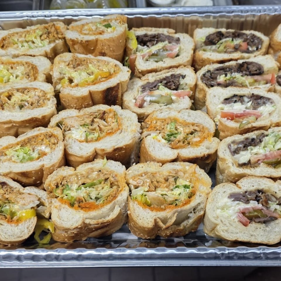 A catering tray filled with AlBasha Subs' sliced sub sandwiches, some chicken and some steak.