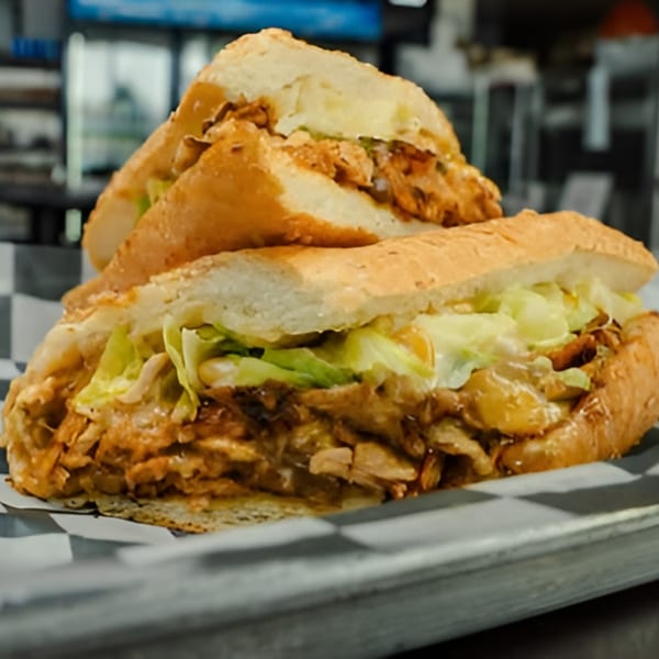 Two halves of a chicken sub sandwich with lettuce and sauce on a checkered paper-lined tray.