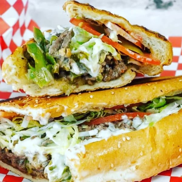 Two halves of a grilled sub sandwich filled with meat, lettuce, tomatoes, and white sauce.