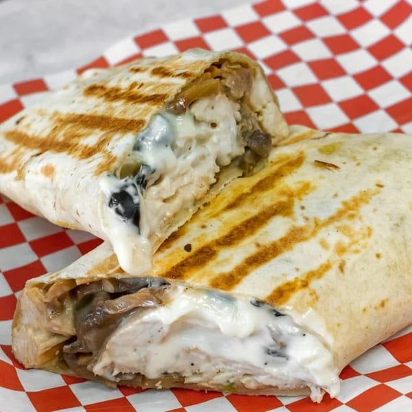 Two grilled chicken and mushroom wraps with creamy sauce on red and white checkered paper.