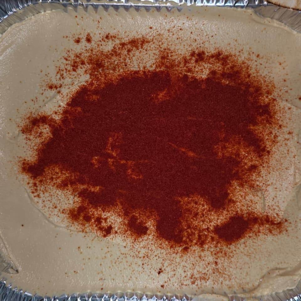 Creamy hummus in a foil container, generously topped with red paprika or sumac spice.