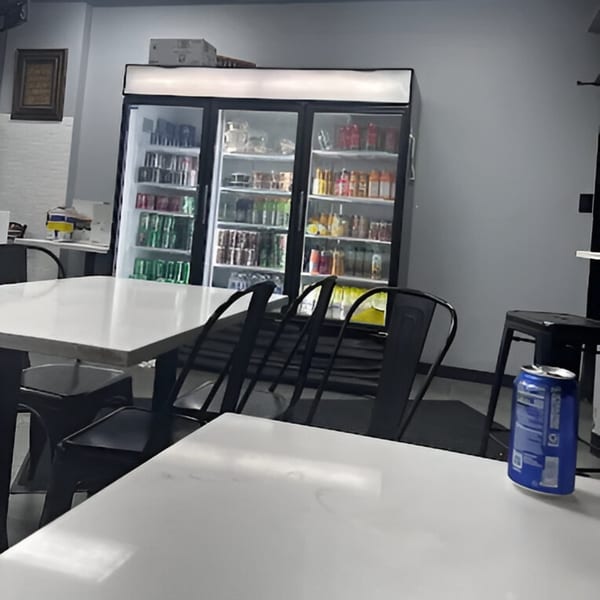 Interior of AlBasha Subs with white tables, black chairs, and a large beverage cooler.