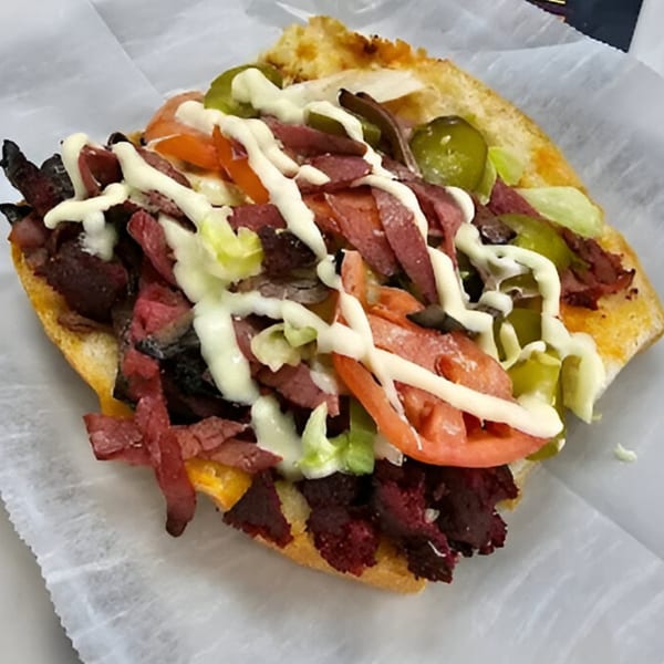 AlBasha Subs' sub sandwich, filled with meat, lettuce, tomatoes, pickles, and drizzled with sauce.