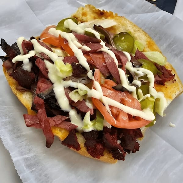 AlBasha Subs' loaded sub sandwich with meat, lettuce, tomatoes, pickles, and white sauce on a bun.