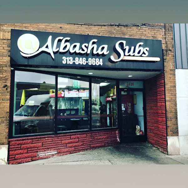 Exterior of AlBasha Subs, a sub-sandwich restaurant with a black sign and red brick facade.