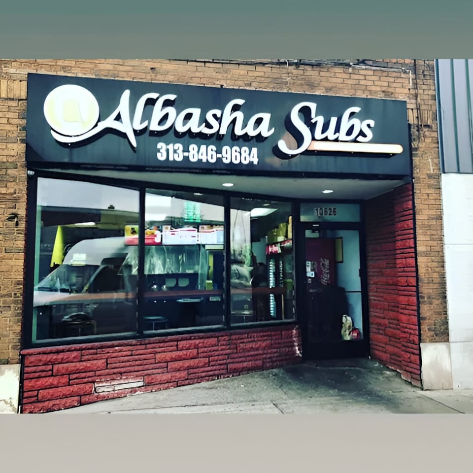 Exterior of AlBasha Subs, a sub-sandwich restaurant with a black sign and red brick facade.