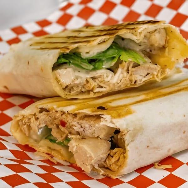 Two halves of a grilled chicken shawarma wrap with lettuce, served on red and white checkered paper.