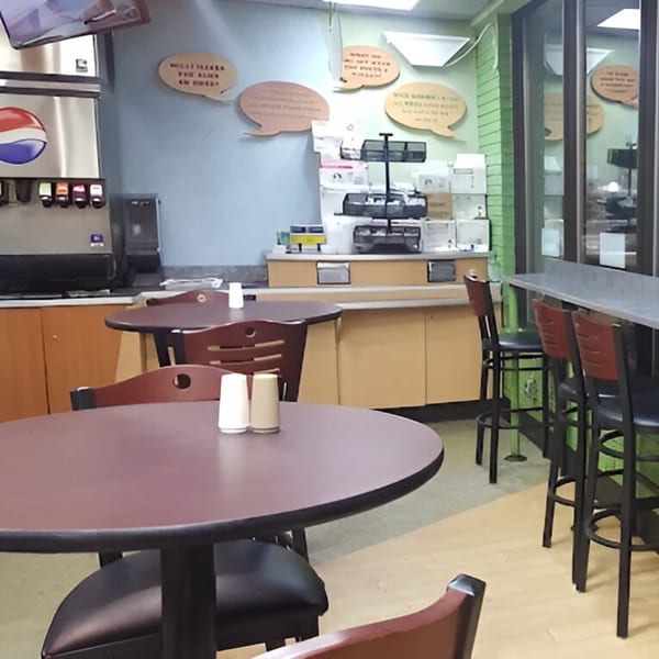 Interior of AlBasha Subs with empty tables, chairs, a soda fountain, and wall decor.
