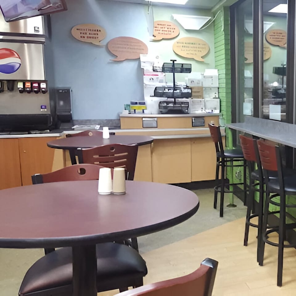 Interior of AlBasha Subs with empty tables, chairs, a soda fountain, and wall decor.
